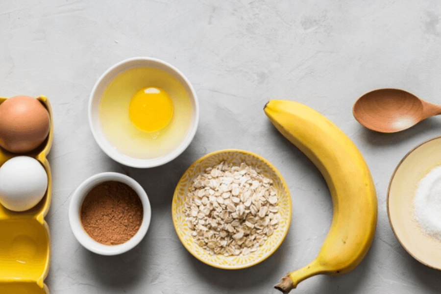 A bowl of banana bread batter with mashed bananas, flour, eggs, and a whisk, ready to be poured into a loaf pan.